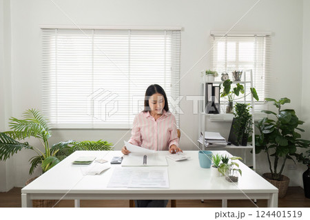 Home Office and Document Management. An individual sorting through paperwork while seated in a bright home office. Home Office and Document Management. An individual sorting through paperwork while seated in a bright home office. 124401519