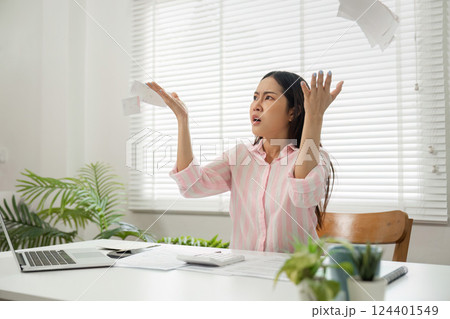 Overwhelmed by Financial Stress. A woman expresses her frustration by throwing papers in her home office. 124401549
