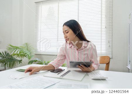 Remote Work and Document Review. A woman strategizes her tasks while reviewing papers and utilizing tech tools in her home office. Remote Work and Document Review. A woman strategizes her tasks while reviewing papers and utilizing tech tools in her home office. 124401564