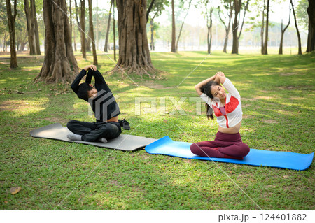 Young couple stretching during morning yoga session on grassy ground in a park Young couple stretching during morning yoga session on grassy ground in a park 124401882