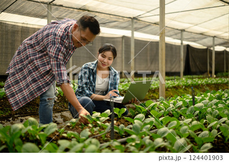 Two young farmers in a greenhouse analyzing crop data on laptop. Modern agriculture concept Two young farmers in a greenhouse analyzing crop data on laptop. Modern agriculture concept 124401903