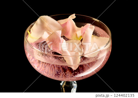 Flower petal cocktail against black background. Chic rose-flavored cocktail with delicate pink petals and sparkling soda in elegant glass. Flower petal cocktail against black background. Chic rose-flavored cocktail with delicate pink petals and sparkling soda in elegant glass. 124402135