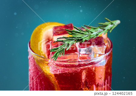 Close-up of cocktail with rosemary and grapefruit on teal background. Refreshing cocktail topped with ice cubes, garnished with rosemary and citrus. Close-up of cocktail with rosemary and grapefruit on teal background. Refreshing cocktail topped with ice cubes, garnished with rosemary and citrus. 124402165