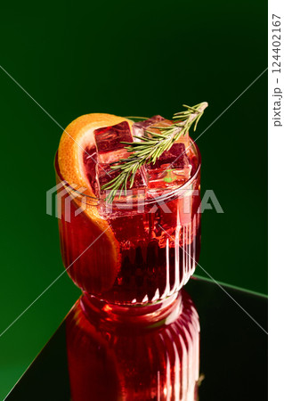 Negroni cocktail with ice cubes, grapefruit slice and rosemary against green studio background. Concept of party 124402167