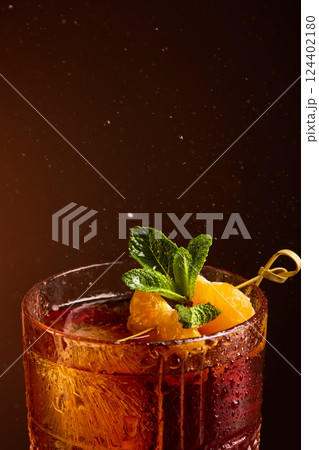 Closeup of Negroni cocktail with mint and citrus covered in water droplets under warm light. 124402180