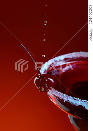 Macro view of cherry cocktail with sugar rim and falling drops creating motion in neon light against gradient background. Macro view of cherry cocktail with sugar rim and falling drops creating motion in neon light against gradient background. 124402208