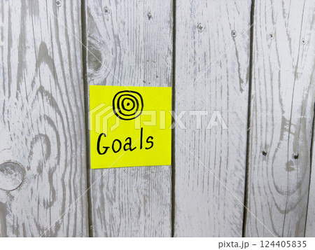 Yellow sticky note featuring the word Goals alongside target symbol, placed on textured wooden background, representing the pursuit of personal aspirations and clear objectives in life Yellow sticky note featuring the word Goals alongside target symbol, placed on textured wooden background, representing the pursuit of personal aspirations and clear objectives in life 124405835