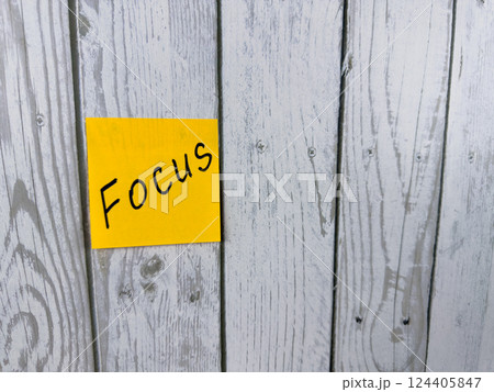 Bright sticky note with the word Focus written on it, pinned on a rustic wooden board background. The image symbolizes concentration, determination, and staying on target Bright sticky note with the word Focus written on it, pinned on a rustic wooden board background. The image symbolizes concentration, determination, and staying on target 124405847