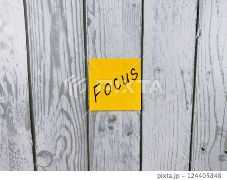Sticky note with the word Focus written on it, placed on a rustic wooden background. Perfect for concepts of concentration, achieving goals, and staying determined in tasks Sticky note with the word Focus written on it, placed on a rustic wooden background. Perfect for concepts of concentration, achieving goals, and staying determined in tasks 124405848