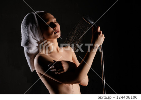 Woman enjoying a refreshing shower while wrapped in a towel in a dimly lit space 124406100
