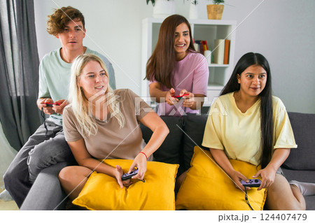 Cheerful group of friends playing video games together at home, leisure and entertainment concept Cheerful group of friends playing video games together at home, leisure and entertainment concept 124407479