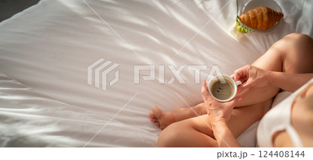 cropped shot of woman holding cup of coffee and croissant on bed cropped shot of woman holding cup of coffee and croissant on bed 124408144