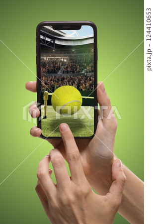Person using smartphone to access tennis sports app, translation of live match updates. Tennis ball and court with filled stands. 124410653