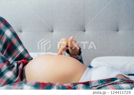 No face Pregnant woman lying on bed, touching her belly, showcasing joy and anticipation. Expecting mother relaxing in pajama during last trimester of pregnancy. Motherhood, preparation, expectation. 124411729