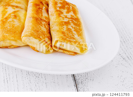 Thin pancakes with filling lying on white plate on wooden table Thin pancakes with filling lying on white plate on wooden table 124411793