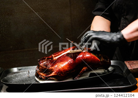 Close up of the chef wearing black gloves cutting and slicing the grilled Peking duck Close up of the chef wearing black gloves cutting and slicing the grilled Peking duck 124412104