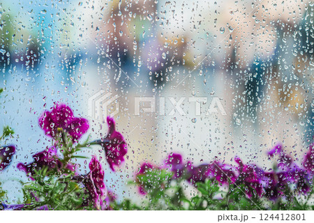 Raindrops on window with purple flowers blurred in background during spring rain. Raindrops create poetic mood, freshness, inspiration and emotional reflection Raindrops on window with purple flowers blurred in background during spring rain. Raindrops create poetic mood, freshness, inspiration and emotional reflection 124412801