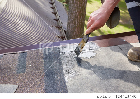 Repair and construction. The hands of the worker apply mastic on the roof of the house. Repair and construction. The hands of the worker apply mastic on the roof of the house. 124413440