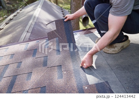 A close-up of the master's hands on the roof mounts flexible tiles. A close-up of the master's hands on the roof mounts flexible tiles. 124413442
