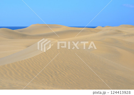 Sand dune with a sea at the background in Maspalomas, Gran Canaria. Sand barkhan with a wavy pattern Sand dune with a sea at the background in Maspalomas, Gran Canaria. Sand barkhan with a wavy pattern 124413928