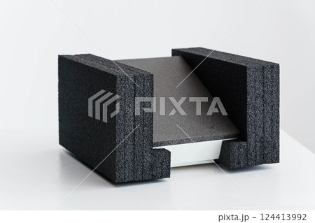 Angular Gray Object Resting Between Two Textured Black Foam Supports on White Surface Angular Gray Object Resting Between Two Textured Black Foam Supports on White Surface 124413992