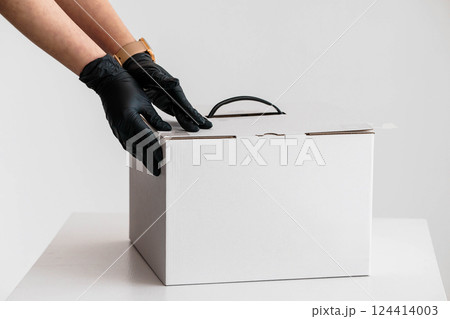 Hands in Black Gloves Carefully Closing White Cardboard Box on White Table 124414003
