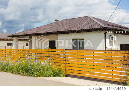 Single-story suburban house behind wooden fence and blooming wildflowers. Home privacy and harmony between architecture and natural surroundings. 124414639