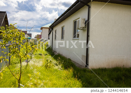 Backyard view of house wall with air conditioner and young trees. Suburban space usage and seasonal landscape development. Backyard view of house wall with air conditioner and young trees. Suburban space usage and seasonal landscape development. 124414654
