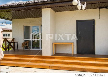 Wooden steps lead to porch with black door and wicker chair. Simple architectural structure and functional outdoor space usage. 124414675