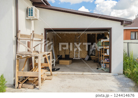 Open garage with tools and wooden planks. Organized storage and efficient use of residential workspace for home maintenance. Open garage with tools and wooden planks. Organized storage and efficient use of residential workspace for home maintenance. 124414676