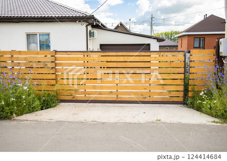 Wooden fence with closed gate and flowers in front of house. Closed access, natural border, and welcoming suburban entrance design 124414684