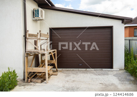 Woodwork and scaffolding in front of brown garage door. Exterior home renovation and tidy, building storage 124414686