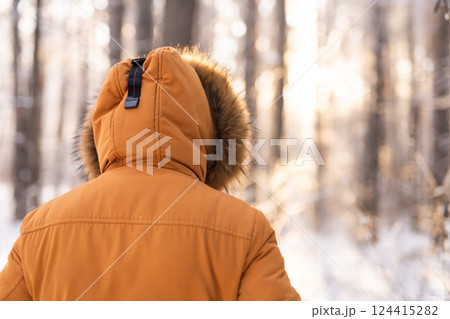 Man walking through snowy forest in warm jacket at sunrise, back view. Solitude, lonely, and connection with winter nature. 124415282