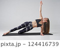 Calm female in activewear doing variation of side plank with bent leg indoors. Side view of barefoot sportswoman practicing side plank yoga position, isolated on grey background. Yoga concept. 124416739