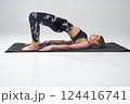 Mindful slim woman in leggings doing bridge position of yoga. Side view of barefoot female in activewear in Setu Bandhasana yoga pose on mat, during training, isolated on grey. Concept of yoga.  124416741