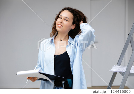 A young pretty girl designer keeps documents while standing at her workplace. Apartment renovation and design concept A young pretty girl designer keeps documents while standing at her workplace. Apartment renovation and design concept 124416809