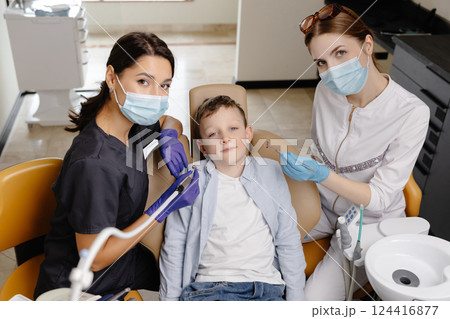 Kid in dental office. Dentist doing hygienic teeth cleaning to a boy sitting in a chair Kid in dental office. Dentist doing hygienic teeth cleaning to a boy sitting in a chair 124416877