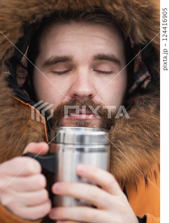 Close-up portrait handsome bearded millennial man in winter clothes and with thermos snow in city . Cold season and hot beverage in winter time 124416905