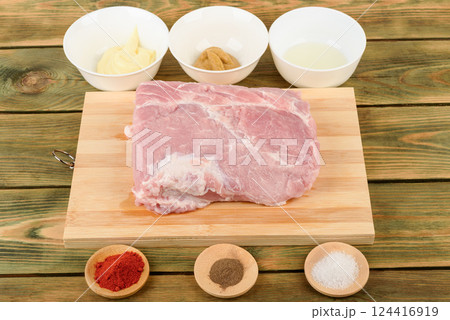 Raw pork meat on a cutting board and spices for marinade. 124416919