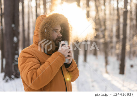 Man warming up with thermos drink in snowy winter forest. Comfort and morning mindfulness in cold natural surroundings 124416937