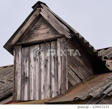 Weathered wooden dormer window on an old tiled roof. The aged wood and peeling paint 124417235