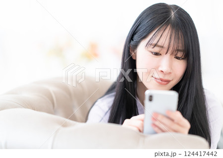 寝そべって自宅でスマホを操作する若い女性 124417442