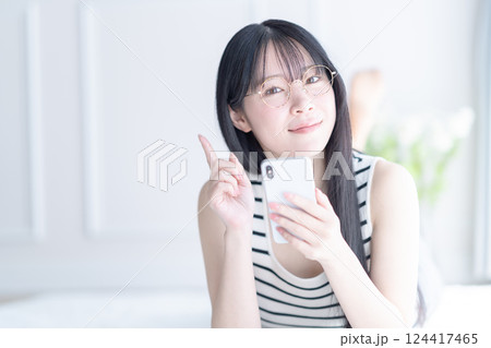 寝そべってスマホを操作するメガネをかけた若い女性 寝そべってスマホを操作するメガネをかけた若い女性 124417465