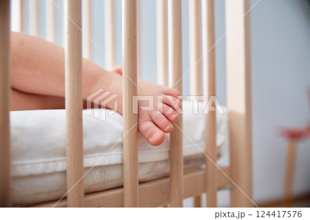 The baby's leg hangs from the child's wooden bed. The baby's leg hangs from the child's wooden bed. 124417576