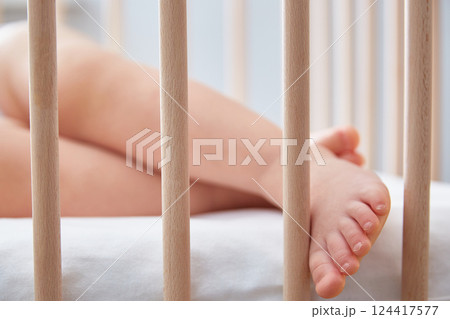 The baby's leg hangs from the child's wooden bed. 124417577