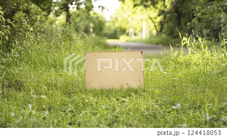 a blank yard sign on a grassy area near a city street path, surrounded by trees and urban elements 124418053