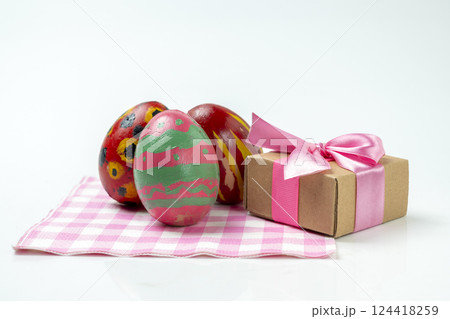 Colorful decorated easter eggs with a gift box on a checkered square cloth isolated over a white background. Concept of celebrating the easter holiday Colorful decorated easter eggs with a gift box on a checkered square cloth isolated over a white background. Concept of celebrating the easter holiday 124418259