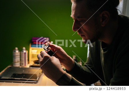 Side view of serious technician carefully replacing smartwatch battery with tweezers, engaging in professional electronics repair workspace. Concept of delicate electronic device maintenance procedure Side view of serious technician carefully replacing smartwatch battery with tweezers, engaging in professional electronics repair workspace. Concept of delicate electronic device maintenance procedure 124418933