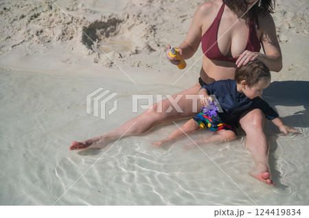 Caucasian woman applies sunscreen to her one-year-old son's skin.  124419834