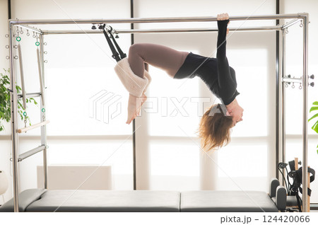Caucasian woman doing aerial exercises on a reformer machine.  124420066